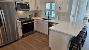 A modern kitchen with stainless steel appliances, white cabinetry, and a large island with bar stools. - Newly renovated in March 2025! 3/2 waterfront pool home! (Marco Island)