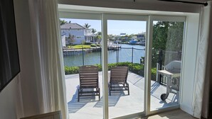 Een balkon met twee houten stoelen, een witte tafel en uitzicht op een jachthaven met boten en huizen.