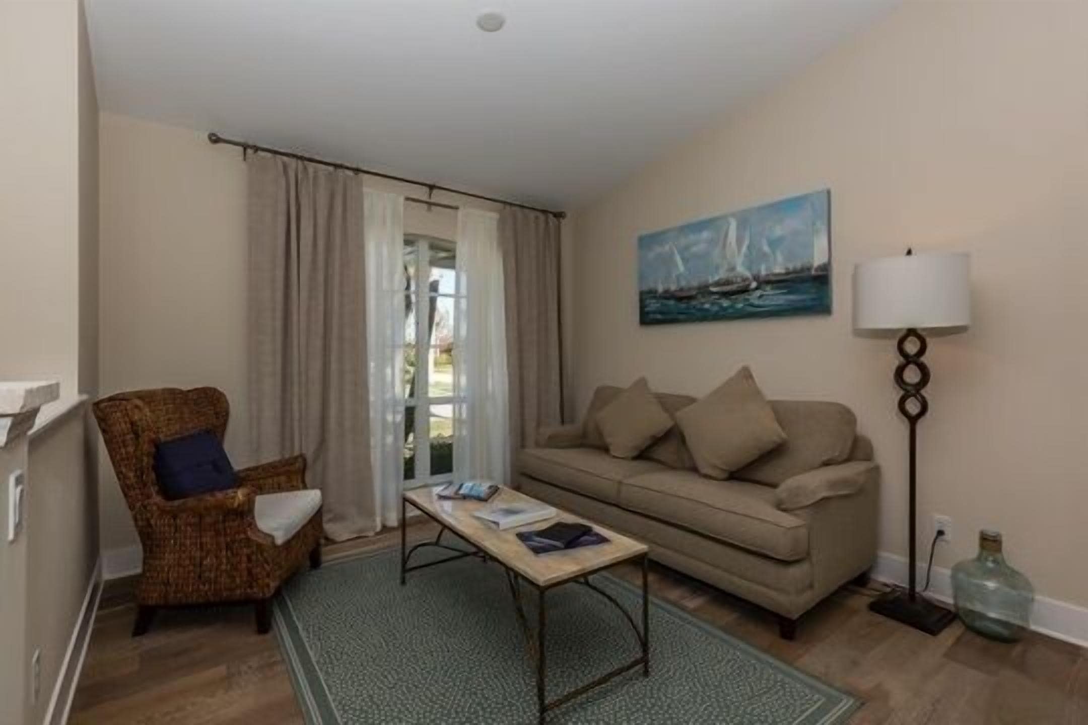 A cozy living room with a sofa, armchair, coffee table, and a painting on the wall.