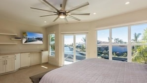 Quarto com uma cama grande, um ventilador de teto e vista para o exterior através de grandes janelas.