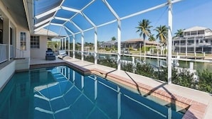 A swimming pool with a glass enclosure, surrounded by palm trees and a clear sky. - Perfect 4/2  home for your Marco Island vacations (Marco Island)
