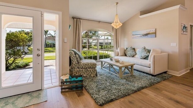 A living room with a sofa, armchair, coffee table, and a view of a garden through a glass door. - Perfect 4/2  home for your Marco Island vacations (Marco Island)