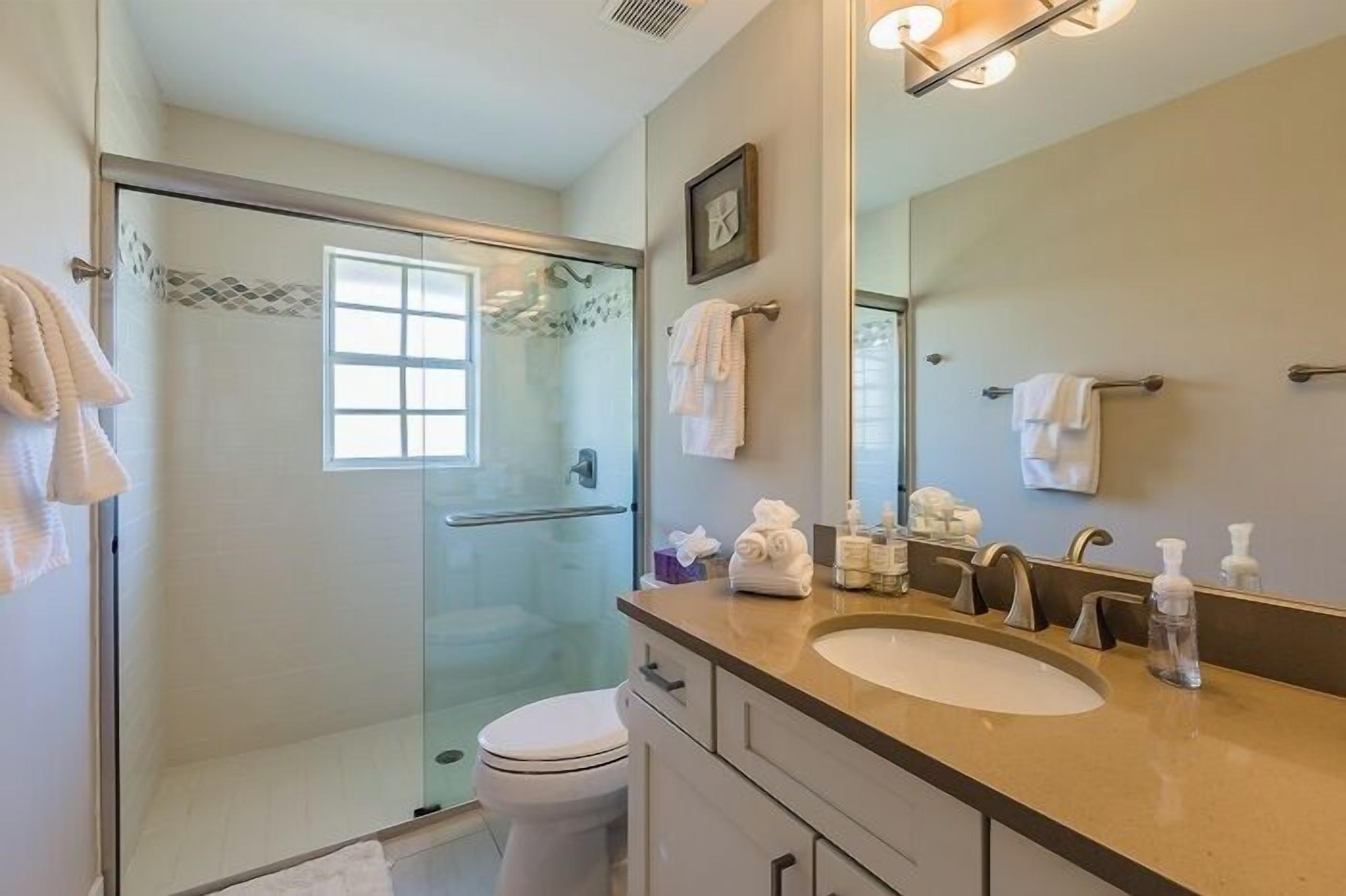 Une salle de bain moderne avec une douche à parois de verre, des toilettes blanches, un meuble-lavabo avec un miroir et un évier, et des serviettes accrochées au mur.