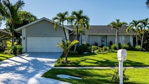 A single-story house with a garage, surrounded by well-maintained lawns and palm trees. - A perfect home to fully enjoy all of Marco Island (Marco Island)