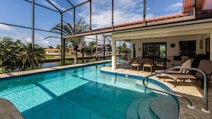 A swimming pool with a glass enclosure, outdoor seating, and a view of palm trees. - 4 bedroom, 3 bath home with heated pool (Marco Island)