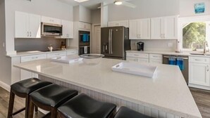 Une cuisine moderne avec des meubles blancs, un grand îlot central doté de tabourets, un four encastré et un réfrigérateur.