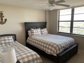 A bedroom with two beds, a ceiling fan, a window with blinds, and a wall-mounted anchor.