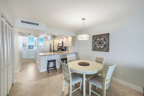 A modern kitchen with a central island, white cabinetry, and a dining area with a round table and chairs. - Beautifully updated  2/2 condo with Gulf views (Marco Island)