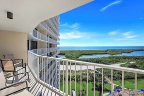 A balcony with a view of a coastal landscape, including a body of water and greenery.