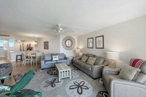 A modern living room with a grey sofa, a dining table, and a kitchen in the background. - Beautifully updated  2/2 condo with Gulf views (Marco Island)
