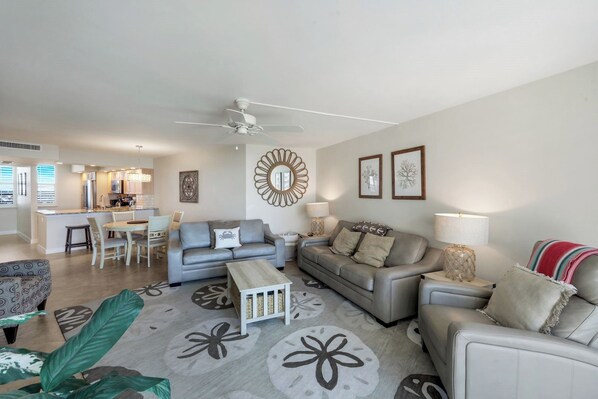 A modern living room with a grey sofa, a dining table, and a kitchen in the background.