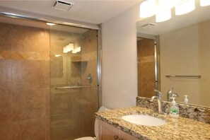 A modern bathroom with a glass-enclosed shower, a granite countertop sink, and a large mirror. - Beautifully updated 2/2 condo with Gulf views (Marco Island)