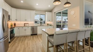 A modern kitchen with white cabinets, stainless steel appliances, and a central island with bar stools. - Beautiful 3Bdr Home located in the heart of Marco. (Marco Island)