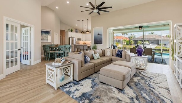 A spacious living room with a sectional sofa, a coffee table, and a large rug. There is a dining area with a table and chairs, and a kitchen in the background. - Beautiful 3Bdr Home located in the heart of Marco. (Marco Island)