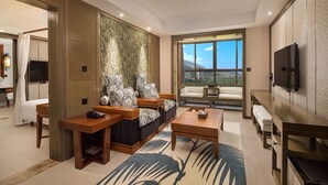 A modern living room with a sofa set, a coffee table, and a TV. There is a large window with a view of a cityscape. - Wyndham Xishuangbanna South Resort (Xishuangbanna Dai)