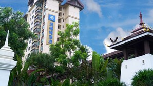A multi-story hotel with a prominent blue sign, surrounded by lush greenery and a traditional temple structure. - Wyndham Xishuangbanna South Resort (Xishuangbanna Dai)