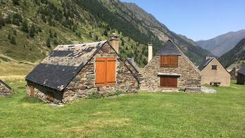 Une petite maison en pierre avec un toit en pente, des volets en bois et une cheminée.