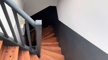 Un escalier en bois avec une rampe métallique, menant à un palier où se trouve un luminaire.