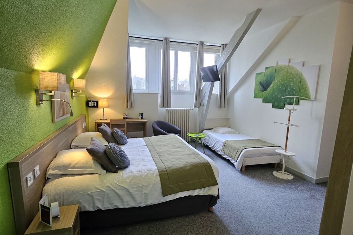 A bedroom with a large bed, a smaller bed, a desk, and a chair. There are windows, a ceiling fan, and artwork on the walls.