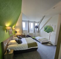 Un dormitorio con una cama grande, una cama más pequeña, un escritorio y una silla. Hay ventanas, un ventilador de techo y obras de arte en las paredes.