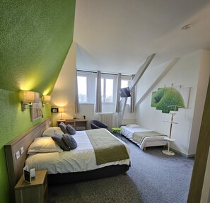 Un dormitorio con una cama grande, una cama más pequeña, un escritorio y una silla. Hay ventanas, un ventilador de techo y obras de arte en las paredes.