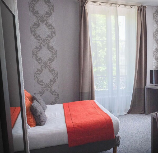 Un dormitorio con cama, cortinas, una ventana y un televisor sobre un mueble.