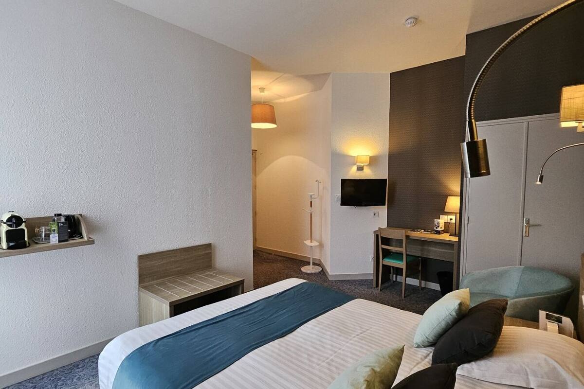 A hotel room with a large bed, bedside tables, a desk, a chair, a wardrobe, and a TV.