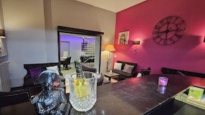A modern living room with a dark brown sofa, a glass table with a bottle, and a clock on the wall.