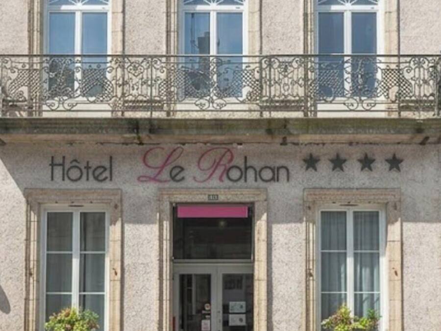 Ein Gebäude mit einem Schild, auf dem 'Hotel Le Rohan' steht, und einem Balkon mit Verziergeländern.