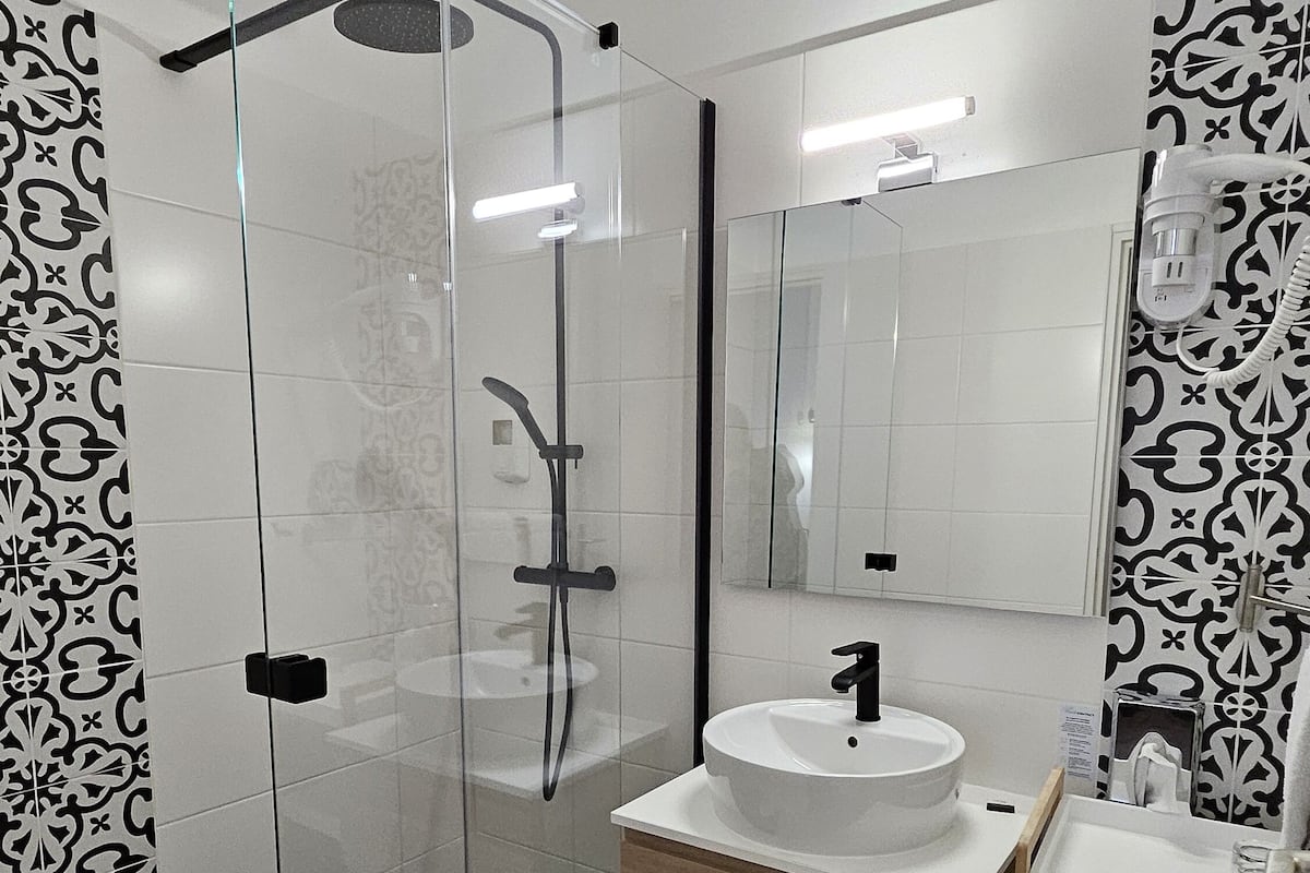 A modern bathroom with a glass shower enclosure, a white sink with a wooden vanity, and a large mirror.