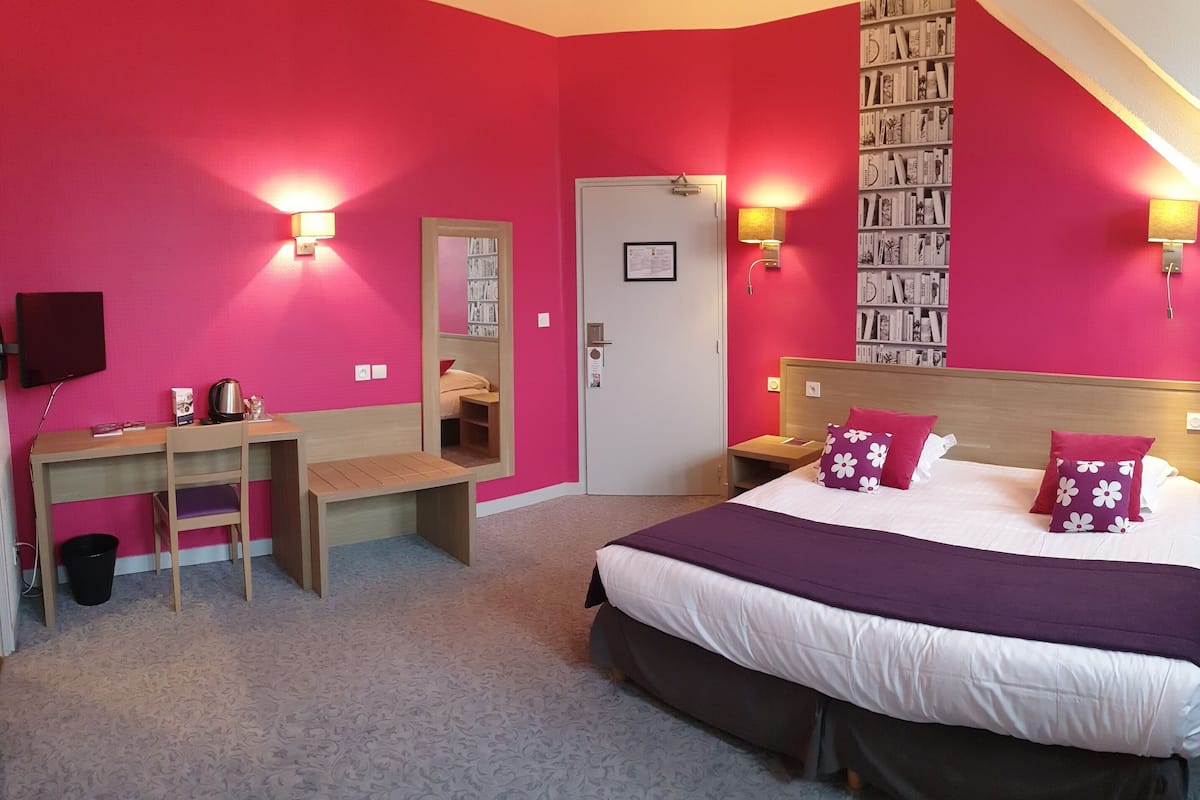 A bedroom with a bed, bedside tables, a desk, a chair, a bookshelf, and a door.