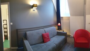 A room with a grey sofa, a red chair, a small table with a lamp, and a wall-mounted light fixture.