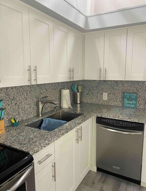 A kitchen with white cabinets, a granite countertop, a stainless steel sink, and a dishwasher.