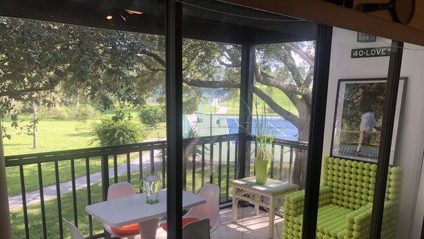 A balcony with a table and chairs, a potted plant, and a tennis court in the background. - Ultimate Tennis Condo at World Tennis Center (Naples)