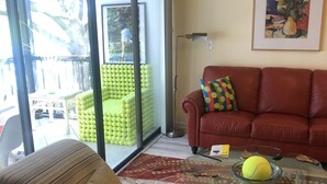 A living room with a glass coffee table, a red sofa, and a green chair. - Ultimate Tennis Condo at World Tennis Center (Naples)