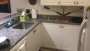 A kitchen with white cabinets, a granite countertop, a sink, a clock, and a striped rug. - Ultimate Tennis Condo at World Tennis Center (Naples)