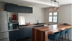 A modern kitchen with dark cabinets, a wooden island, and bar stools. - House 90 m2 sleeps 6 (Le Gosier)