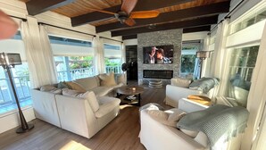 Amplia sala de estar con televisor grande, vigas de madera en el techo y vistas al exterior.