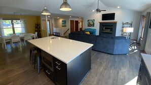 Cozinha moderna com ilha central, área de jantar com cadeiras e sala de estar com sofá e TV.
