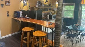 A kitchen with a wooden bar, two stools, a refrigerator, and various kitchen items. - The Cabo Casa (Rogersville)