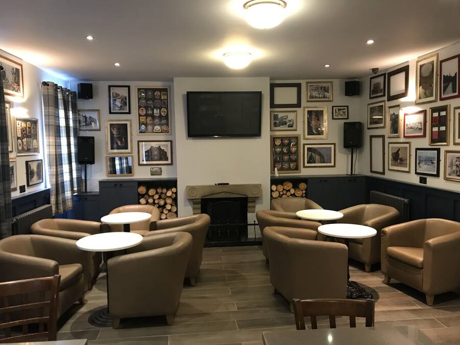 A cozy lounge area with leather armchairs, small round tables, a fireplace, and a wall adorned with framed pictures.