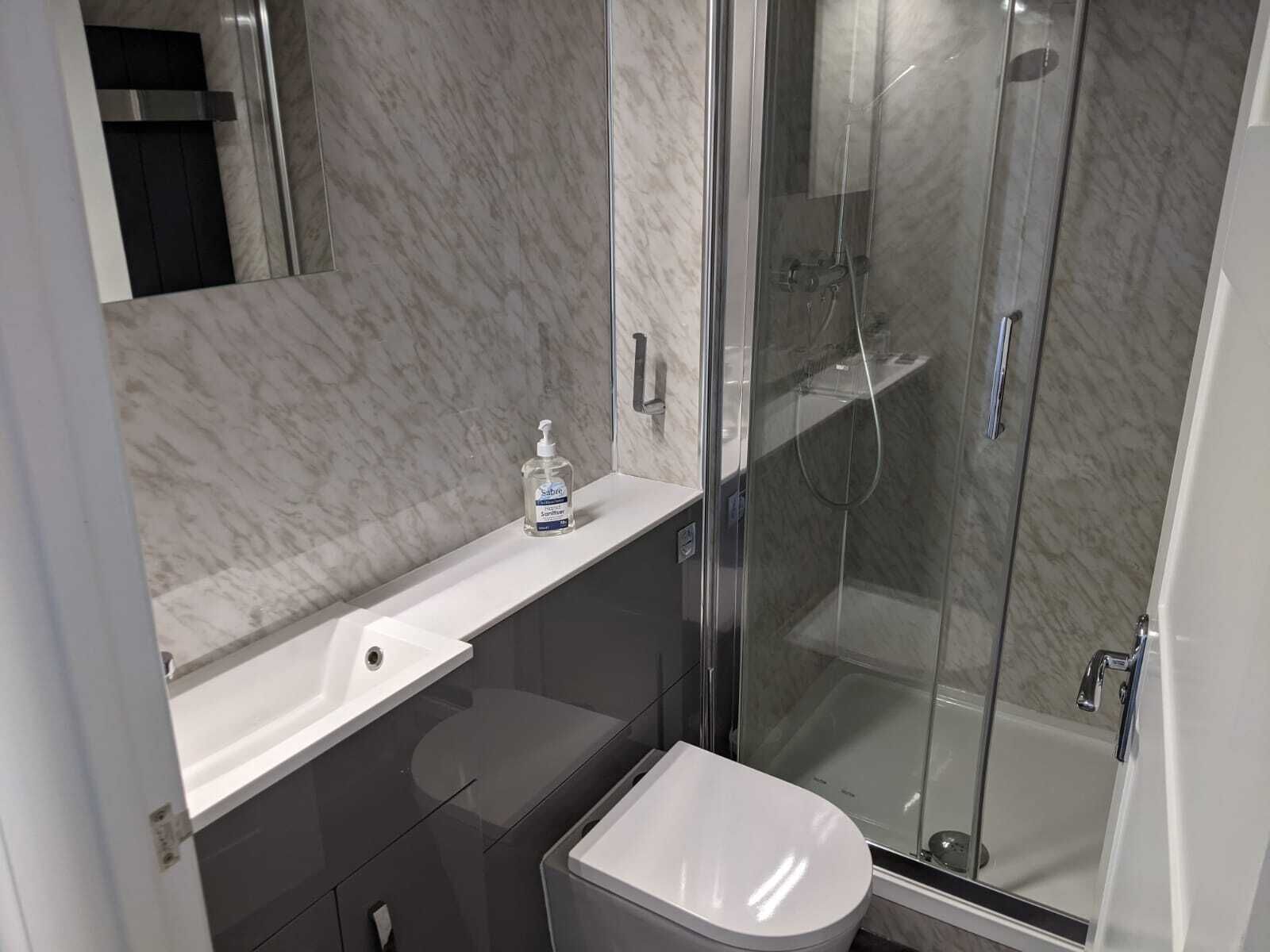 Une salle de bain moderne avec un comptoir en marbre, un lavabo blanc, une douche à parois de verre et des toilettes.
