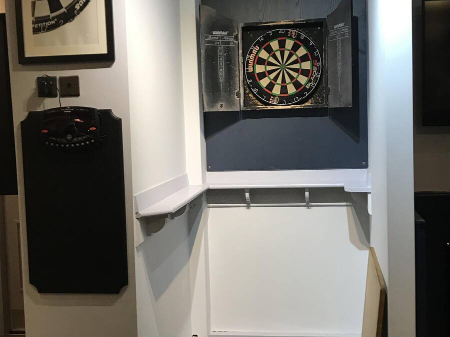 Ein Zimmer mit Dartscheibe an der Wand, einem gerahmten Dartbild und einem Dart-Halter.