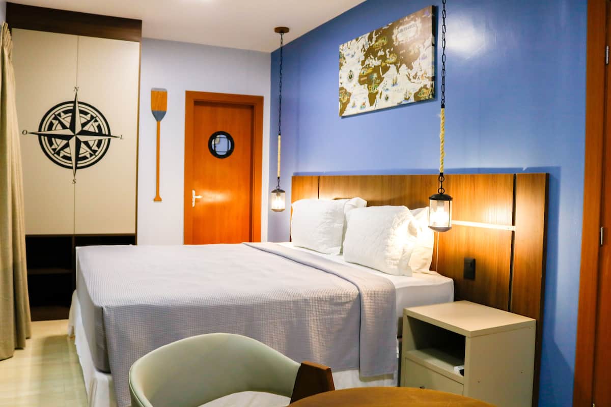 A bedroom with a bed, bedside tables, a chair, a wooden headboard, a wall clock, and a compass decoration.