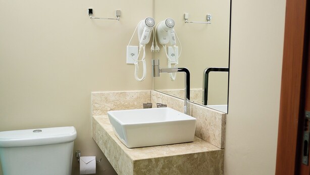 A compact bathroom with a white toilet, a sink with a mirror above it, and a hairdryer on the wall. - Búri Resort (Manaus)