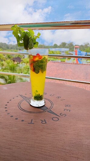 Enjoy a refreshing drink on the balcony with a view of lush greenery and a charming red-roofed structure.