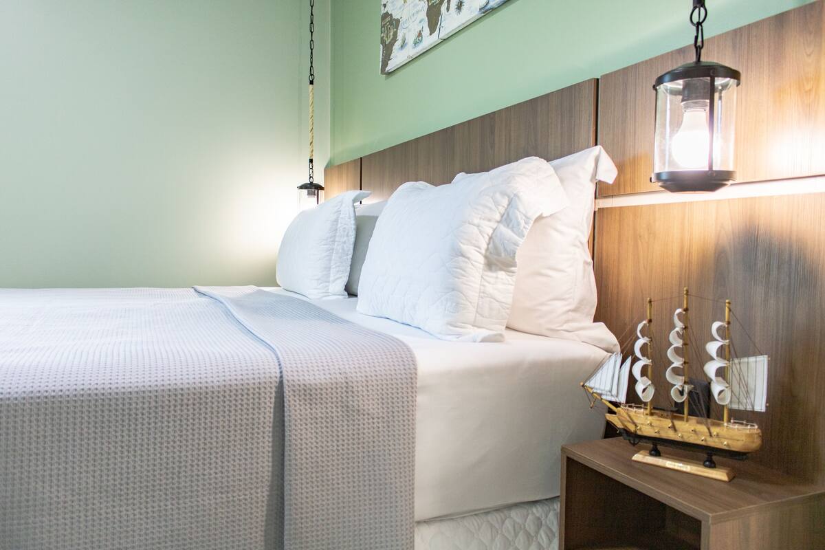 A neatly made bed with white linens, a wooden headboard, and a small wooden nightstand with a ship model.
