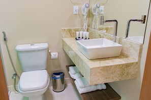 Bathroom features a toilet, sink with countertop, mirror, hair dryers, and a shelf for towels.
