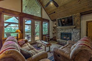 A cozy living room with leather sofas, a stone fireplace, and a large TV.