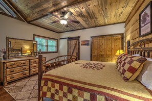 Une chambre à coucher au style rustique, avec un plafond en bois, un lit recouvert d’une courtepointe, une commode et un miroir.